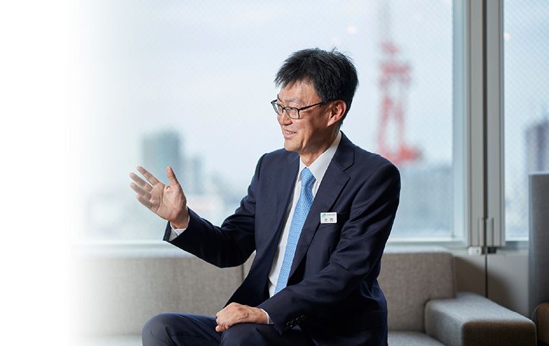 大西 秀麿 社長が窓際のソファに座り、穏やかに談笑する様子